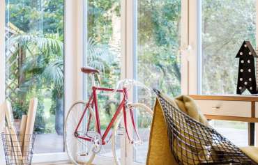 Red and white bike standing by the glass terrace door at home office interior with diamond chair and yellow blanket